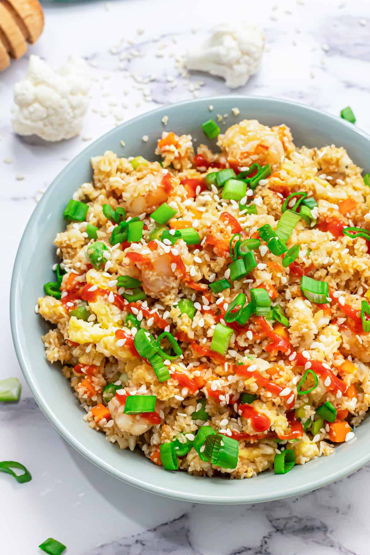 A bowl filled with healthy cauliflower fried rice topped with sriracha and sesame seeds.