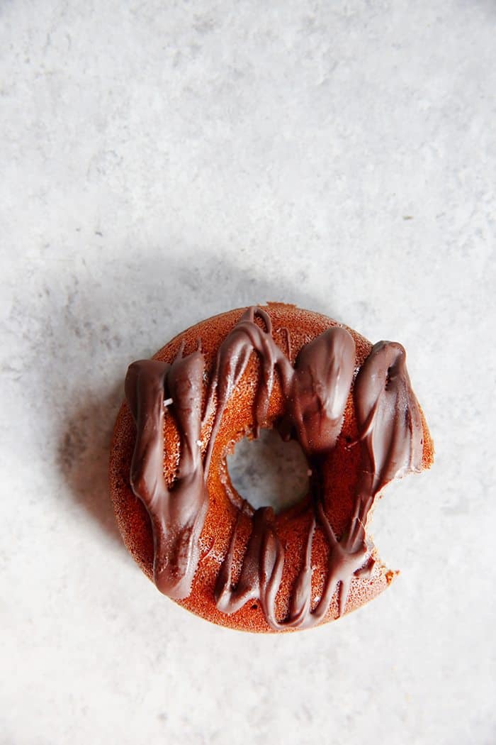 overhead of a chocolate donut drizzled with glaze with a bite taken out