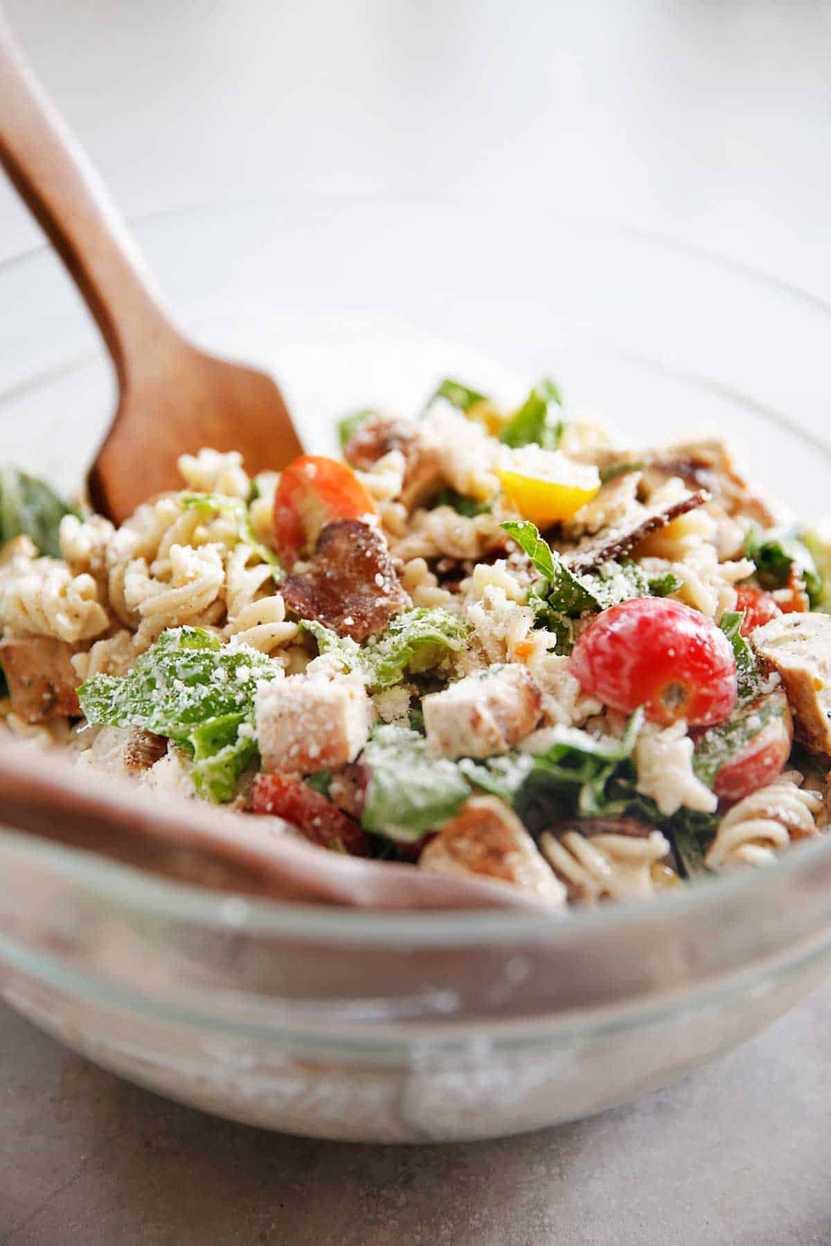 side view of a serving bowl with pasta salad and serving spoons.