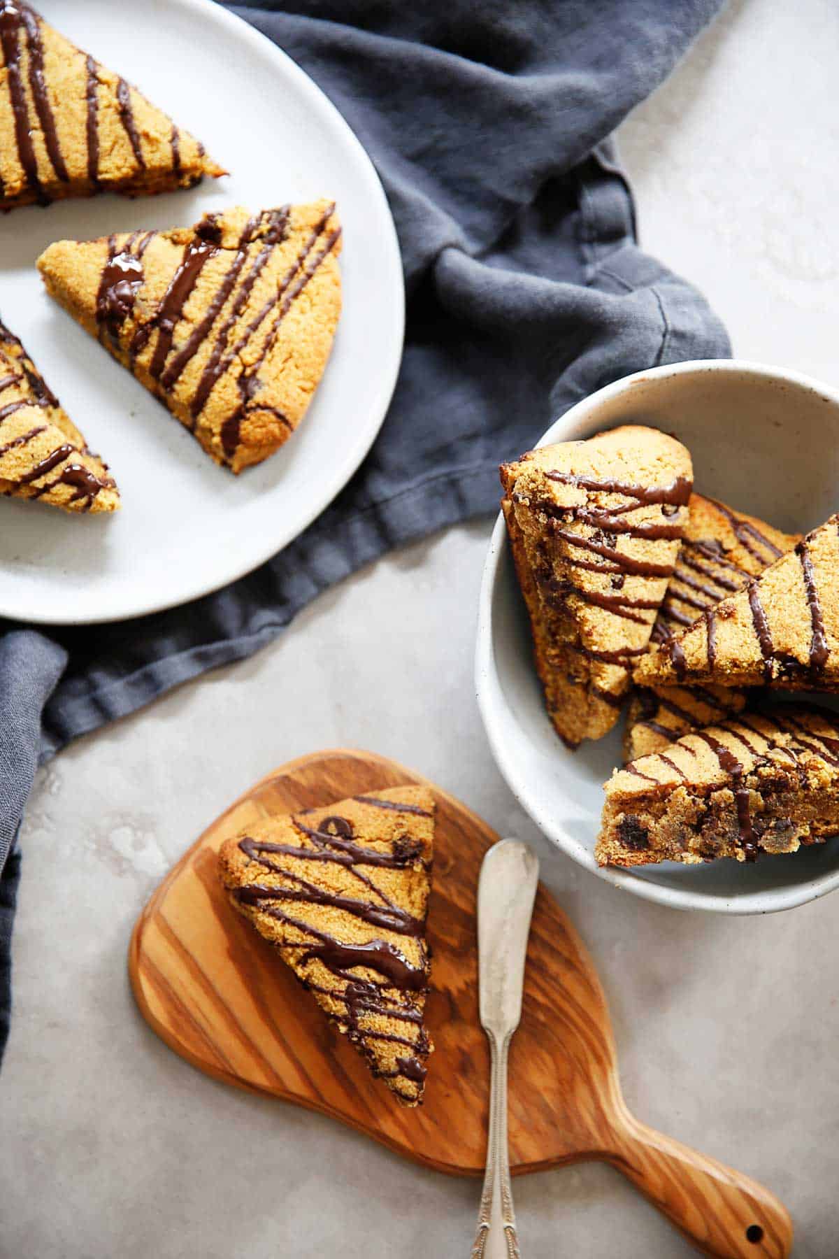 A pumpkin scone with chocolate drizzled over it on a cutting board with a knife.