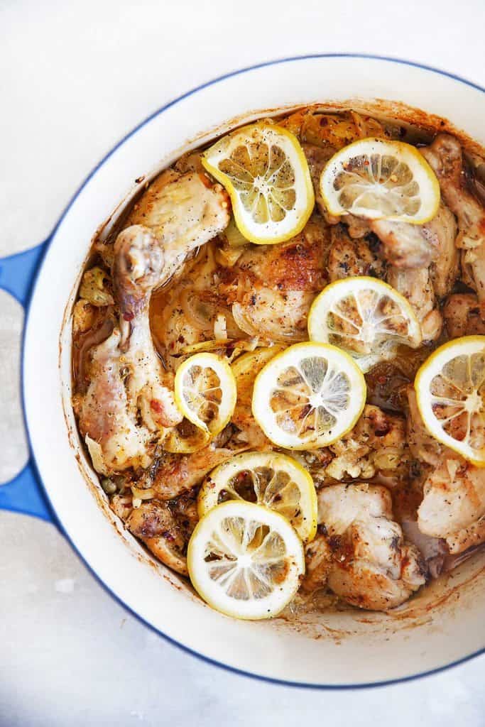 overhead of a Dutch oven with roasted chicken topped with lemon slices.
