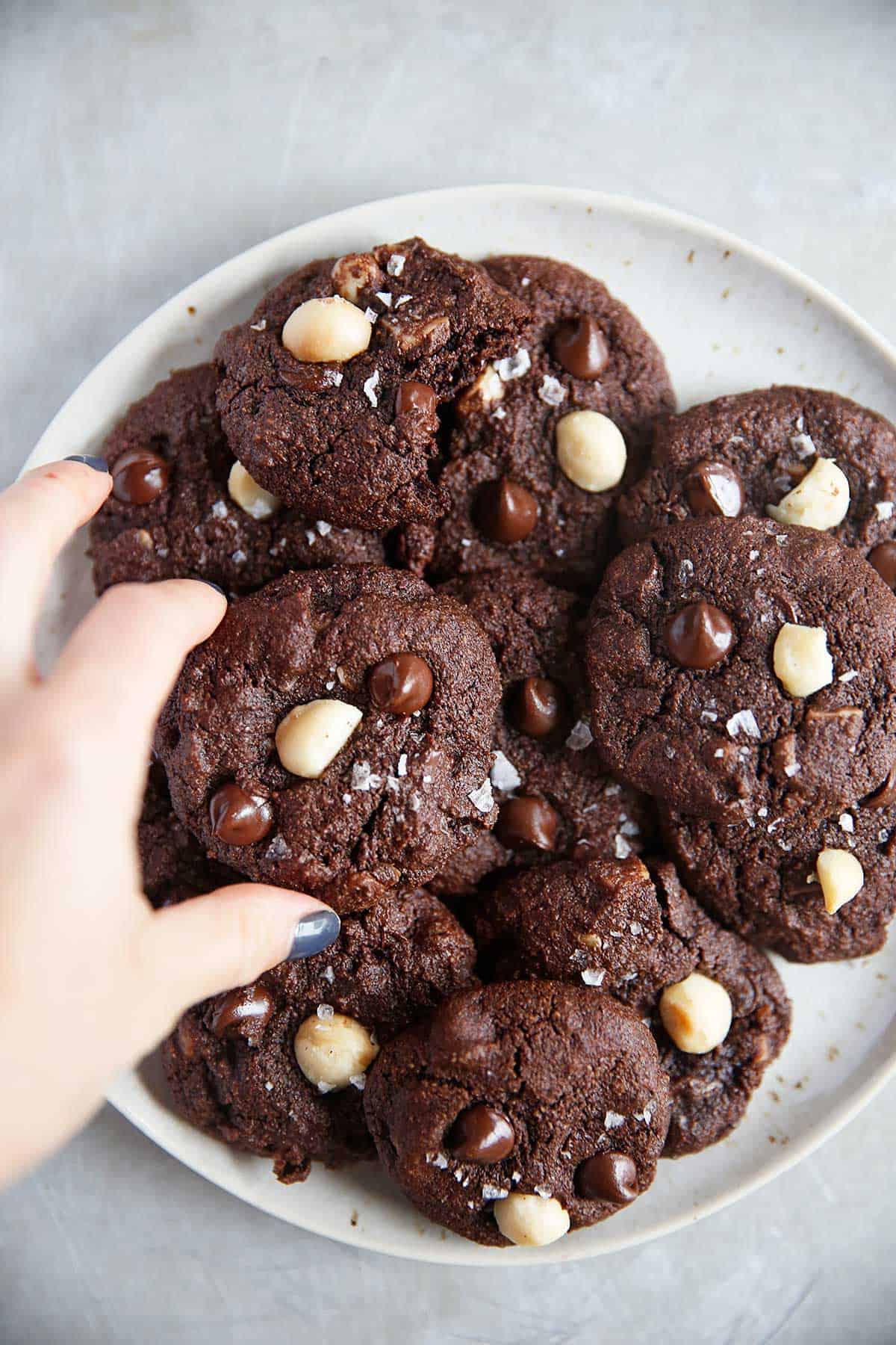 a hand reaching for a platter piled with macadamia cookies.