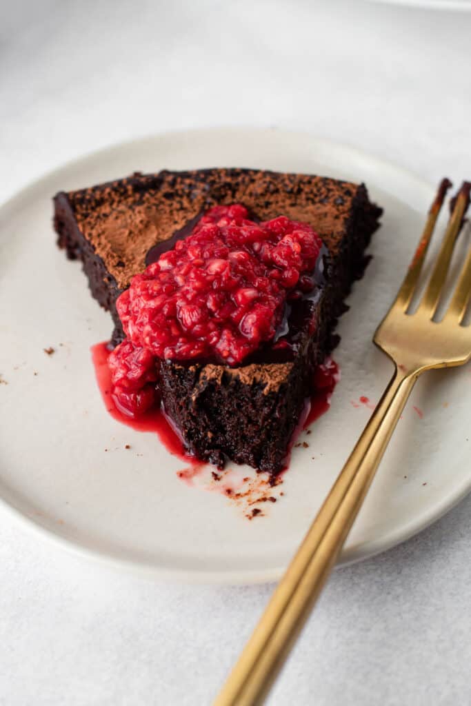 A bite of flourless chocolate cake with a raspberry sauce on top on a plate.