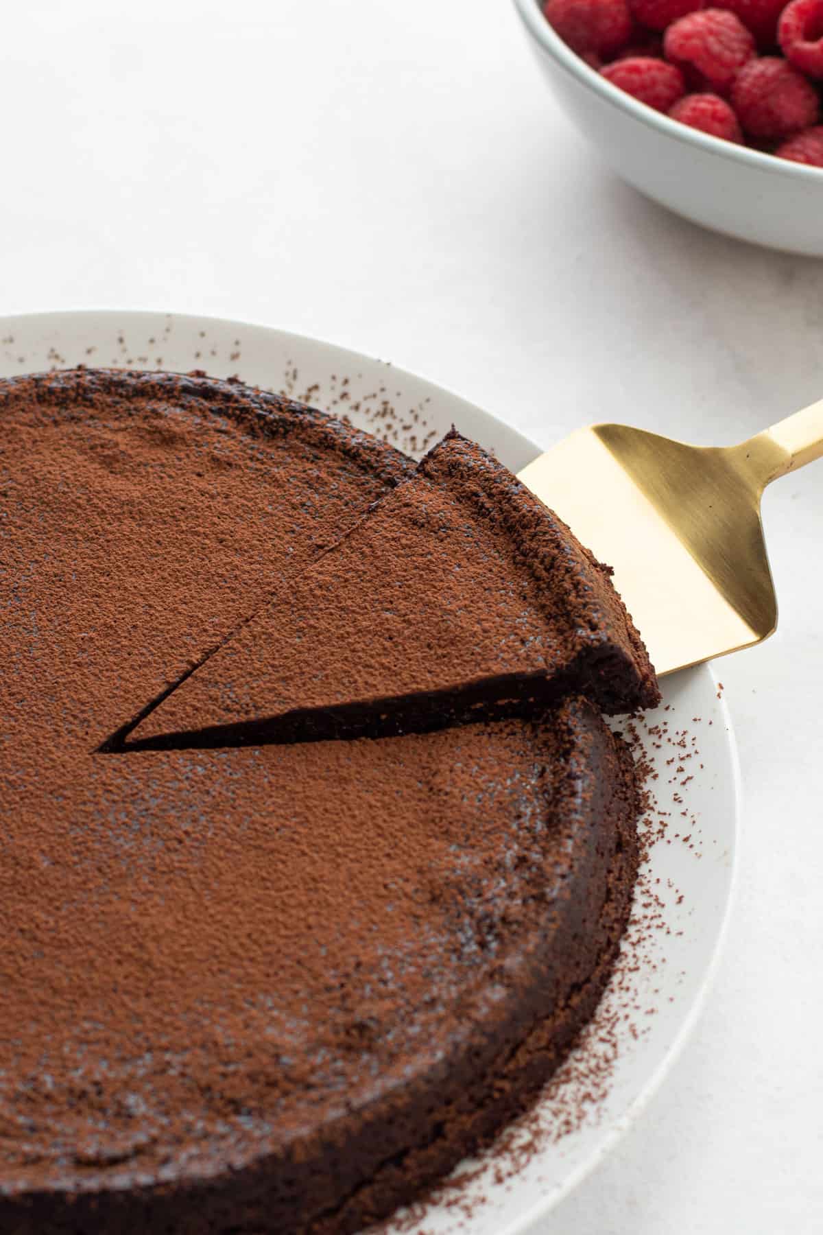 A slice of paleo chocolate cake on a plate with a dusting of cocoa powder on top.