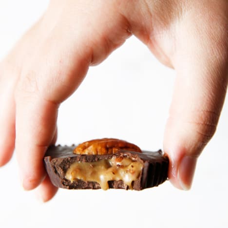 A hand holding a Caramel Chocolate Turtle with a bite taken out of it