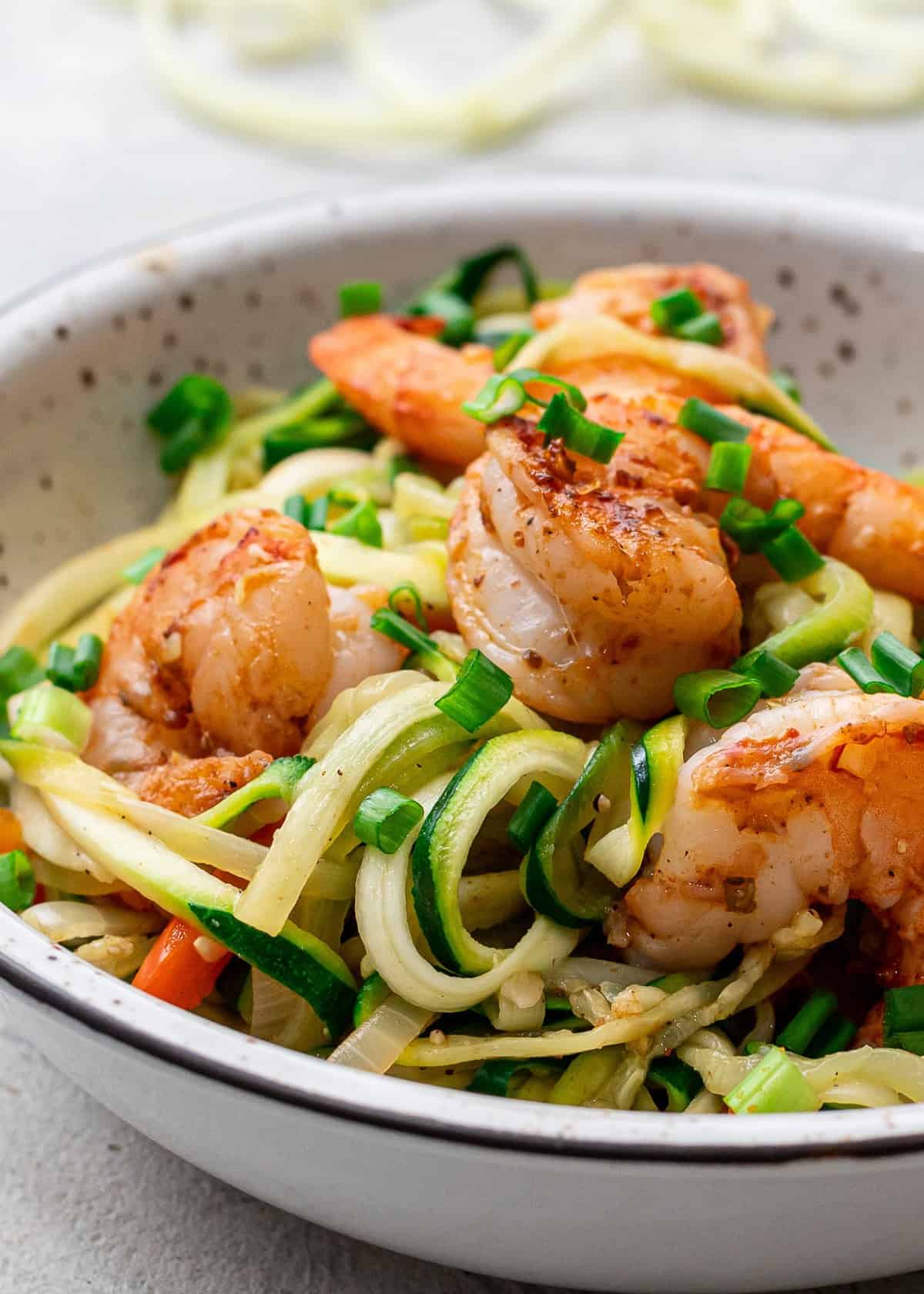 A bowl with zucchini noodles, cajun shrimp and veggies.