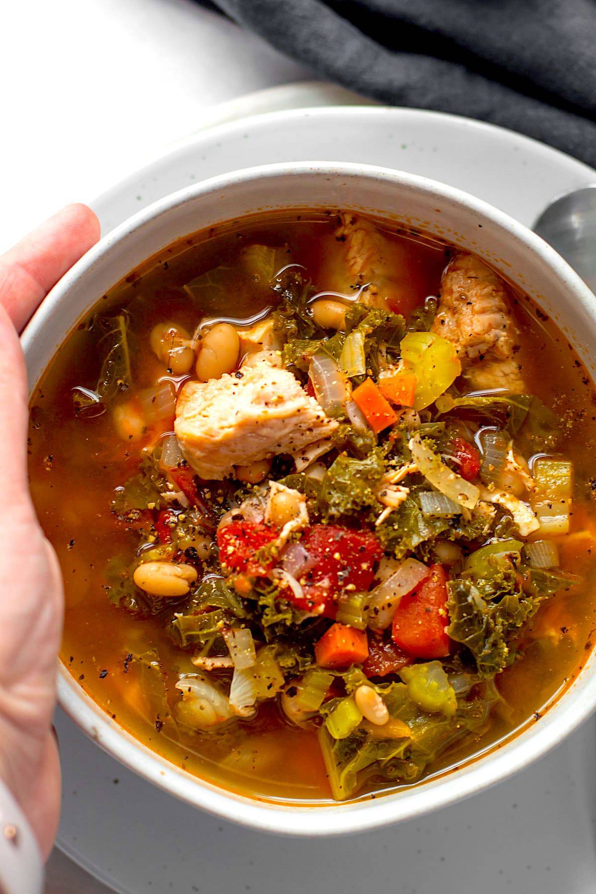 A bowl of turkey kale soup with tomatoes in a bowl.