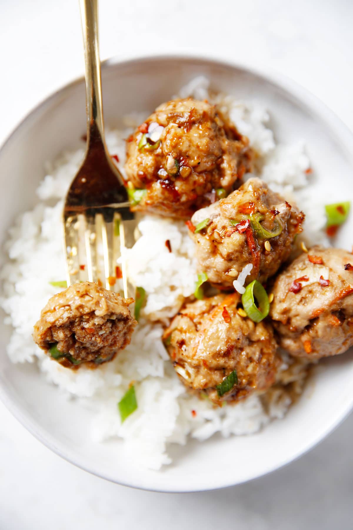 A bowl of rice and Thai meatballs with a fork holding one. 