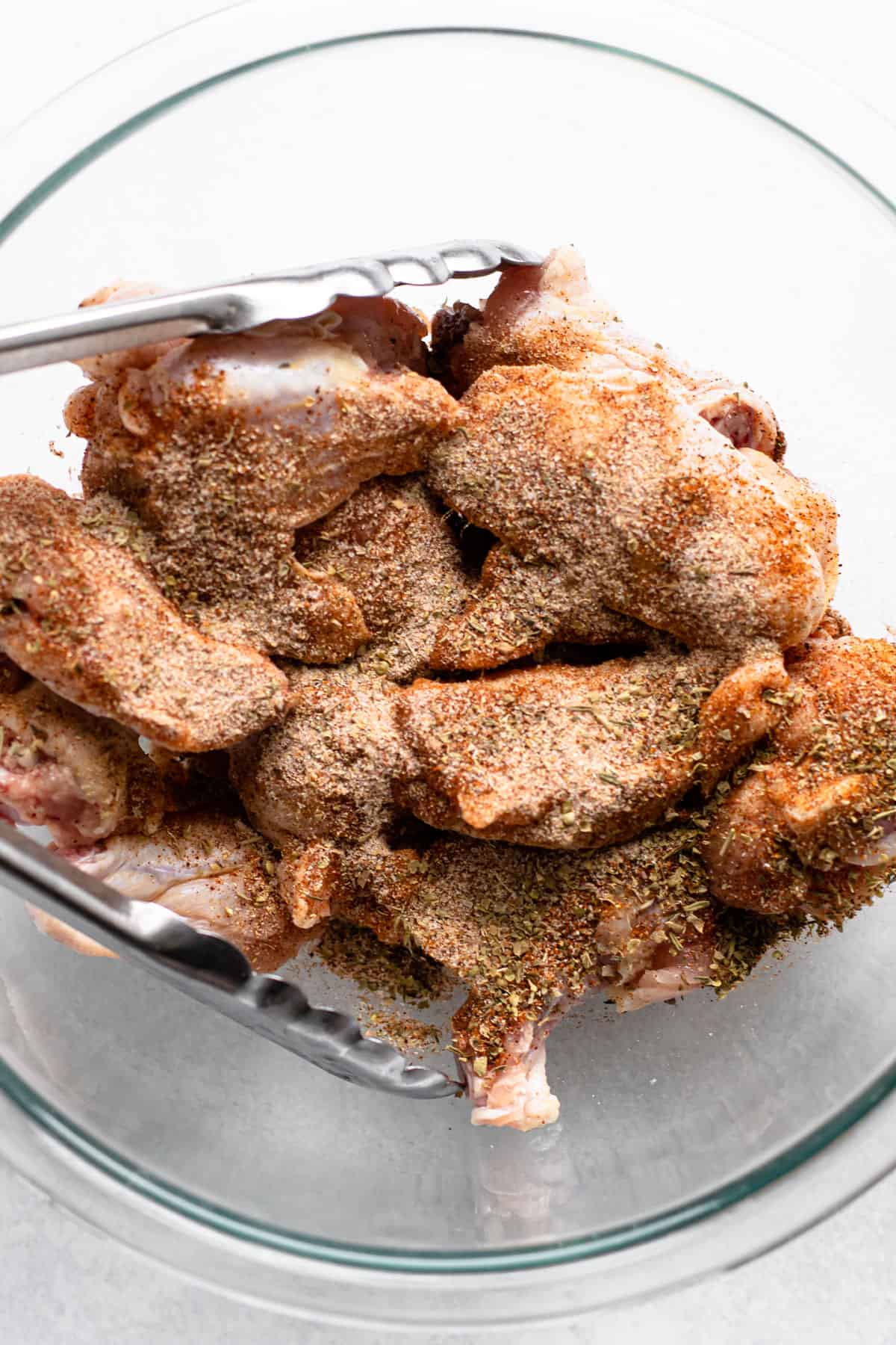 Dry rub ingredients on chicken wings in a bowl.