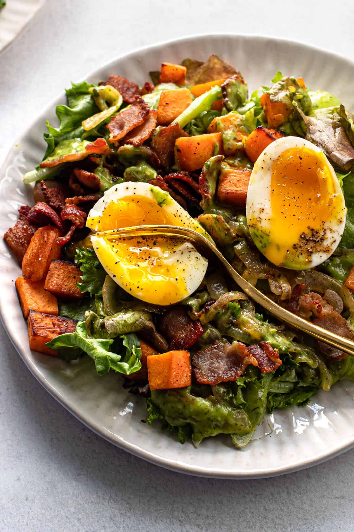 Breakfast salad on a plate topped with a soft-boiled egg.