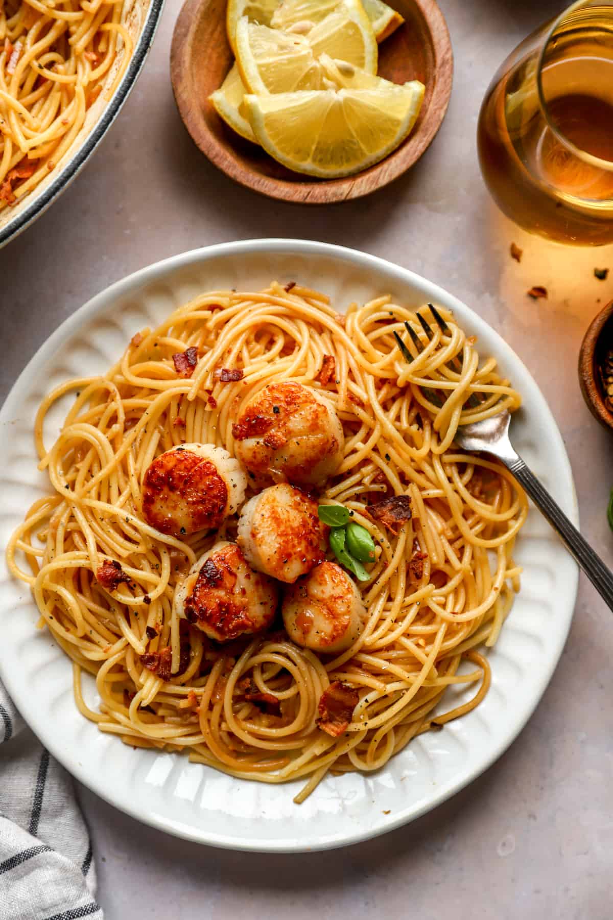 above image of a plate of spaghetti noodles topped with seared scallops and fresh basil.