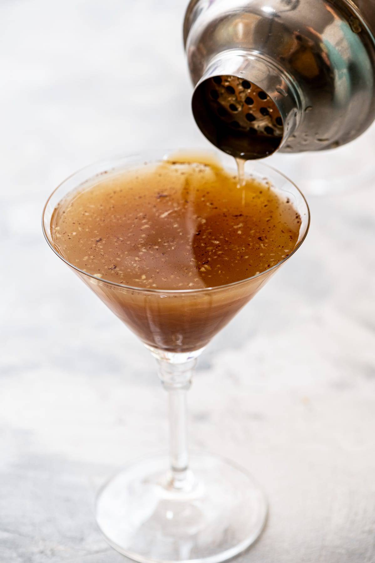Pouring caramel apple martini into a martini glass.