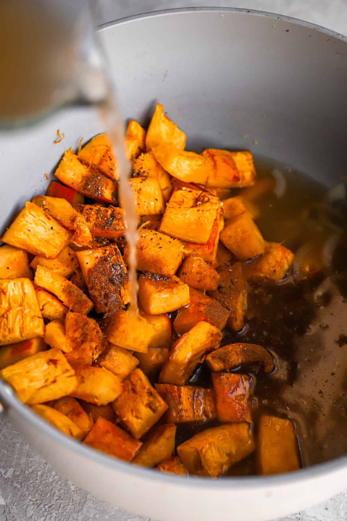 roasted pumpkin cubes in a pot with chicken broth being poured over top.