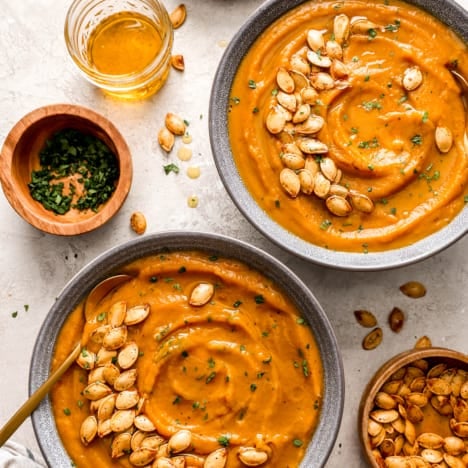 overhead image of two bowls of pumpkin soup topped with roasted pumpkin seeds.