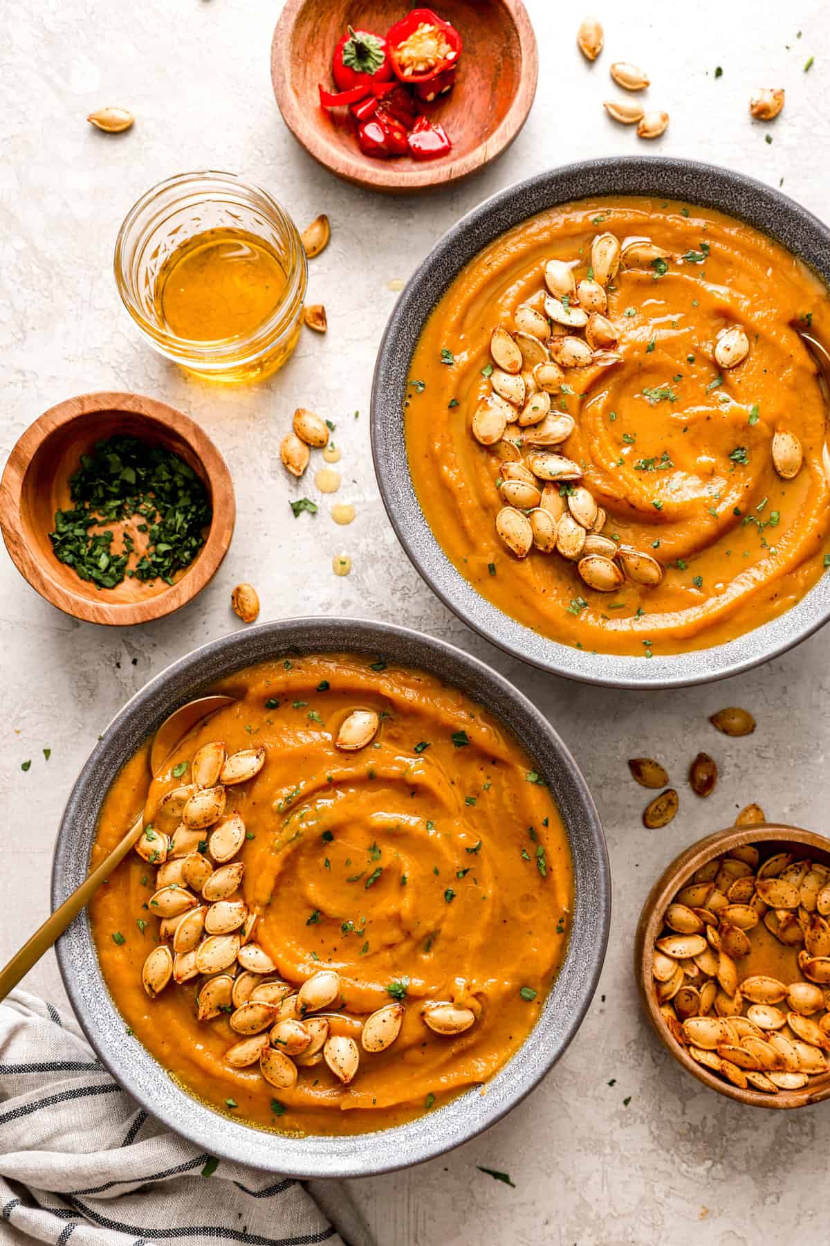 overhead image of two bowls of pumpkin soup topped with roasted pumpkin seeds. 