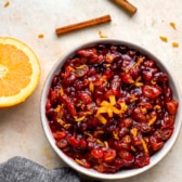 overhead of a bowl filled with cranberry orange relish set next to half of an orange and cinnamon sticks.