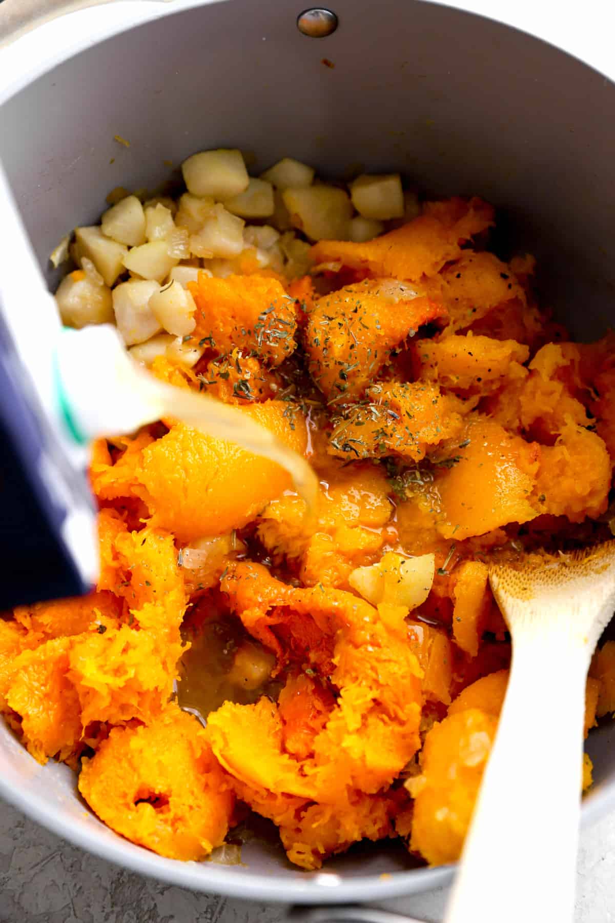 cooked squash being added to a pan for a squash soup recipe.