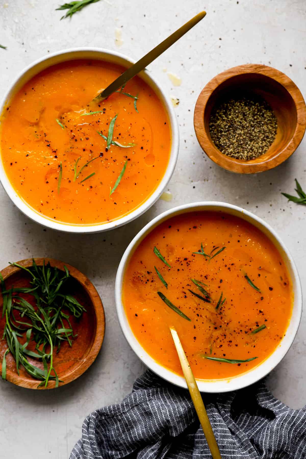 above image of two bowls of French squash soup garnished next to two bowls of fresh tarragon garnish.