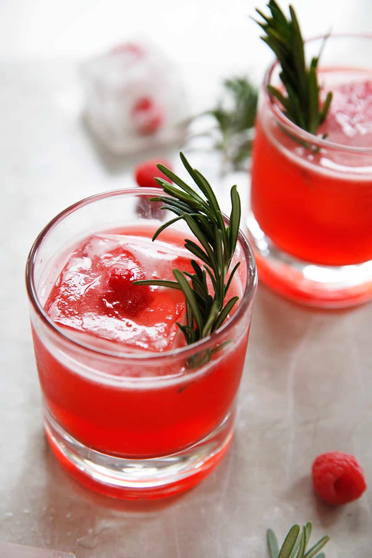 Two glasses with a raspberry gin cocktail and a sprig of rosemary.