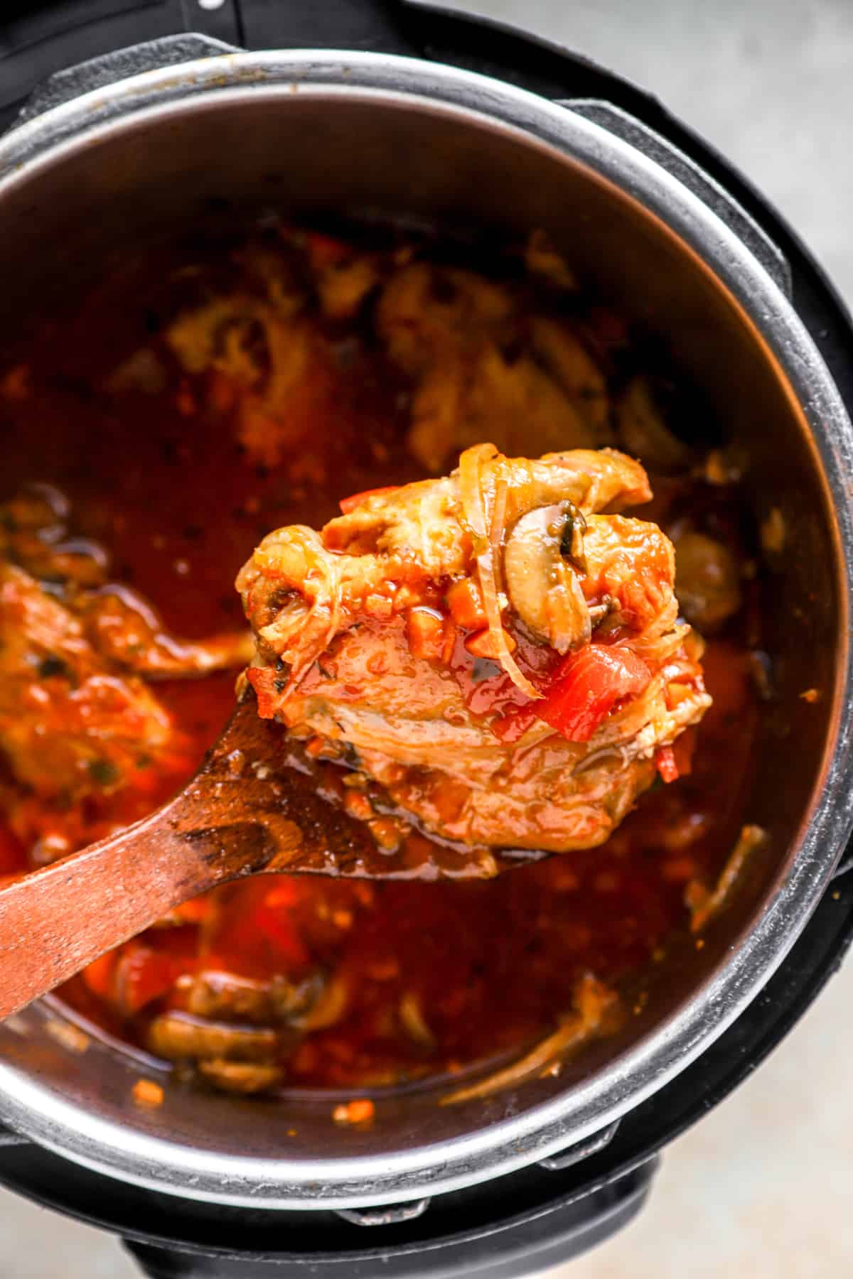 a scoop of chicken cacciatore being held over an instant pot.