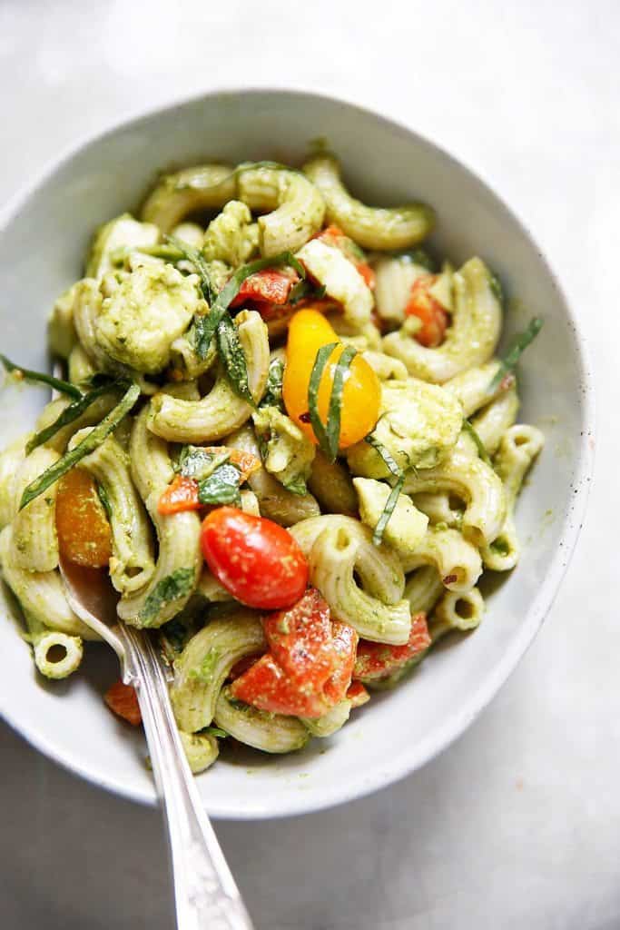 A small serving bowl of pesto pasta with tomato and mozzarella.