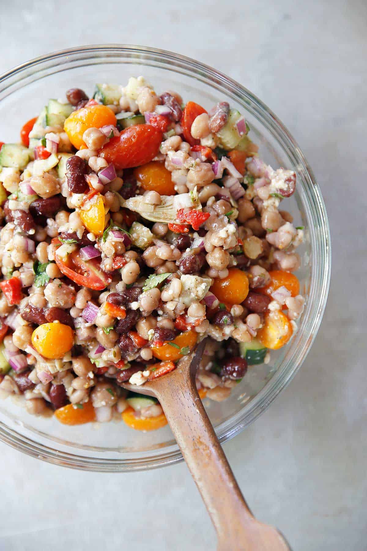 Greek Three Bean Salad in a bowl with a wooden spoon in it.