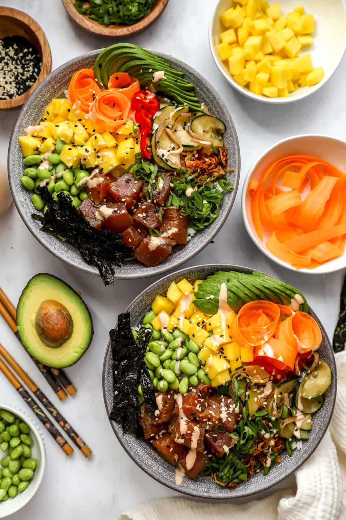 two poke bowls from above surrounded by toppings. 