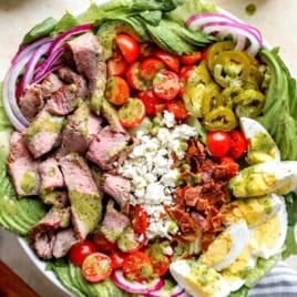 an entire steak cobb salad in a white bowl - think a bed of lettuce, diced cherry tomatoes, diced red onions, sliced hard boiled egg, chopped bacon, sliced steak.