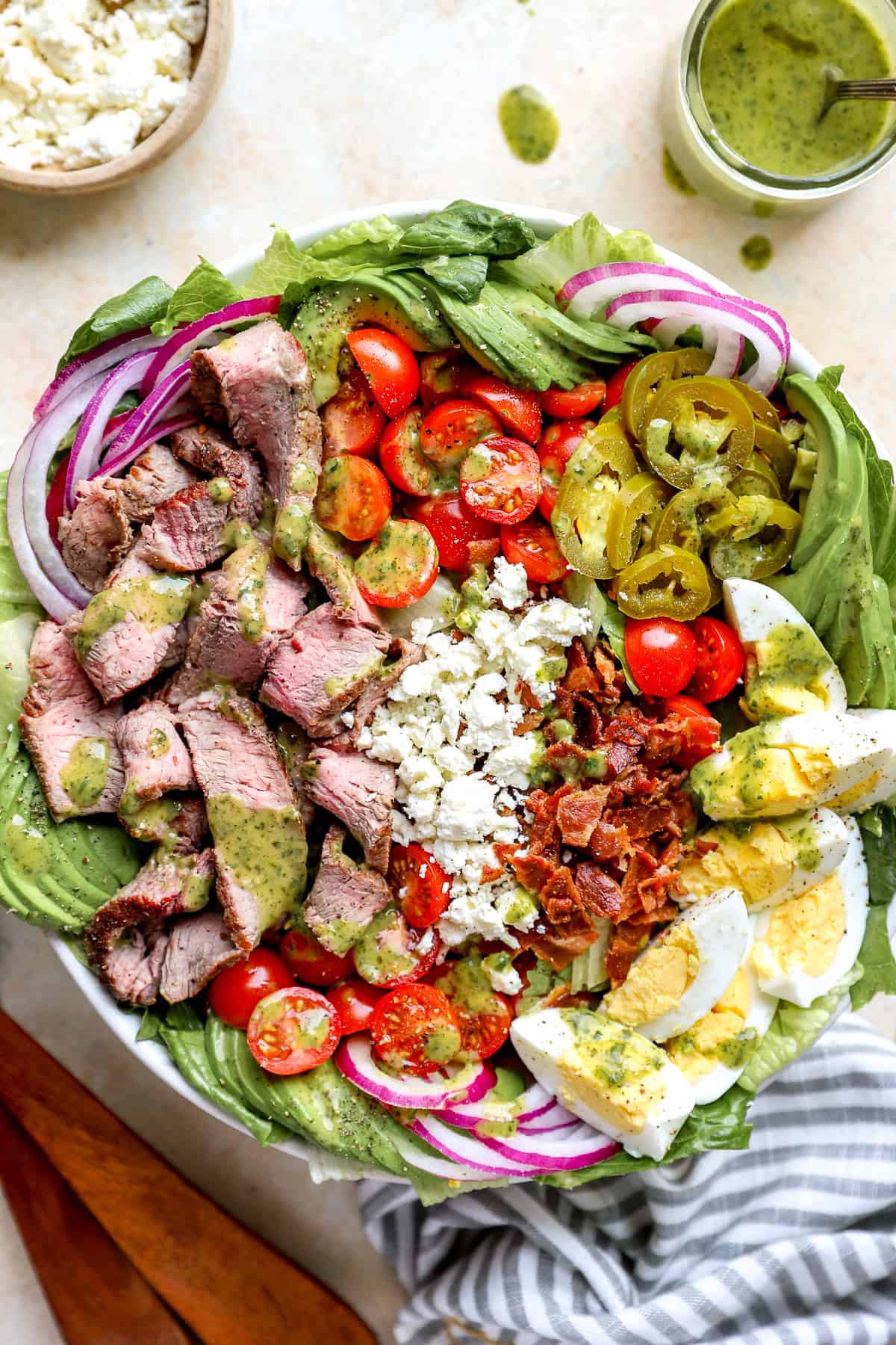 an entire steak cobb salad in a white bowl - think a bed of lettuce, diced cherry tomatoes, diced red onions, sliced hard boiled egg, chopped bacon, sliced steak. 
