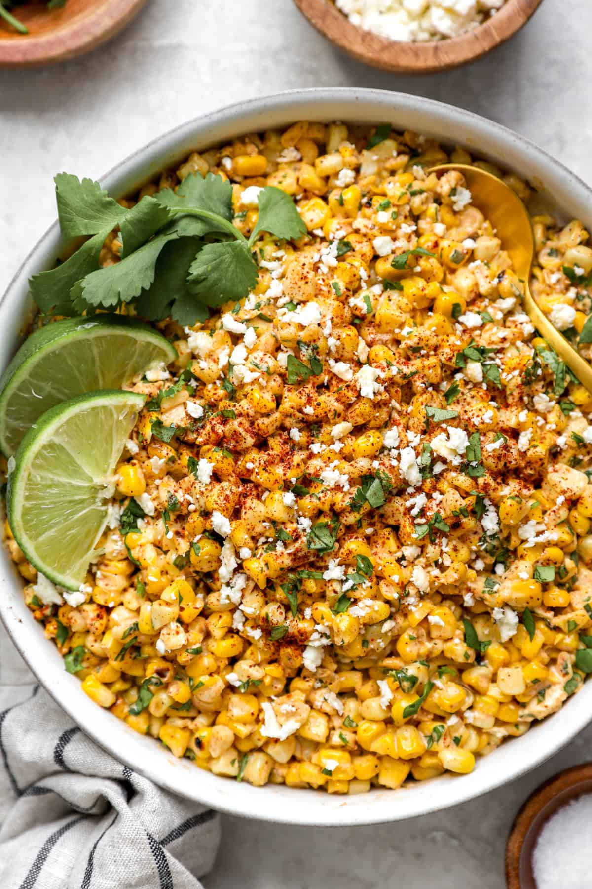 a big bowl of Mexican corn salad from above garnished with cilantro and lime wedges.