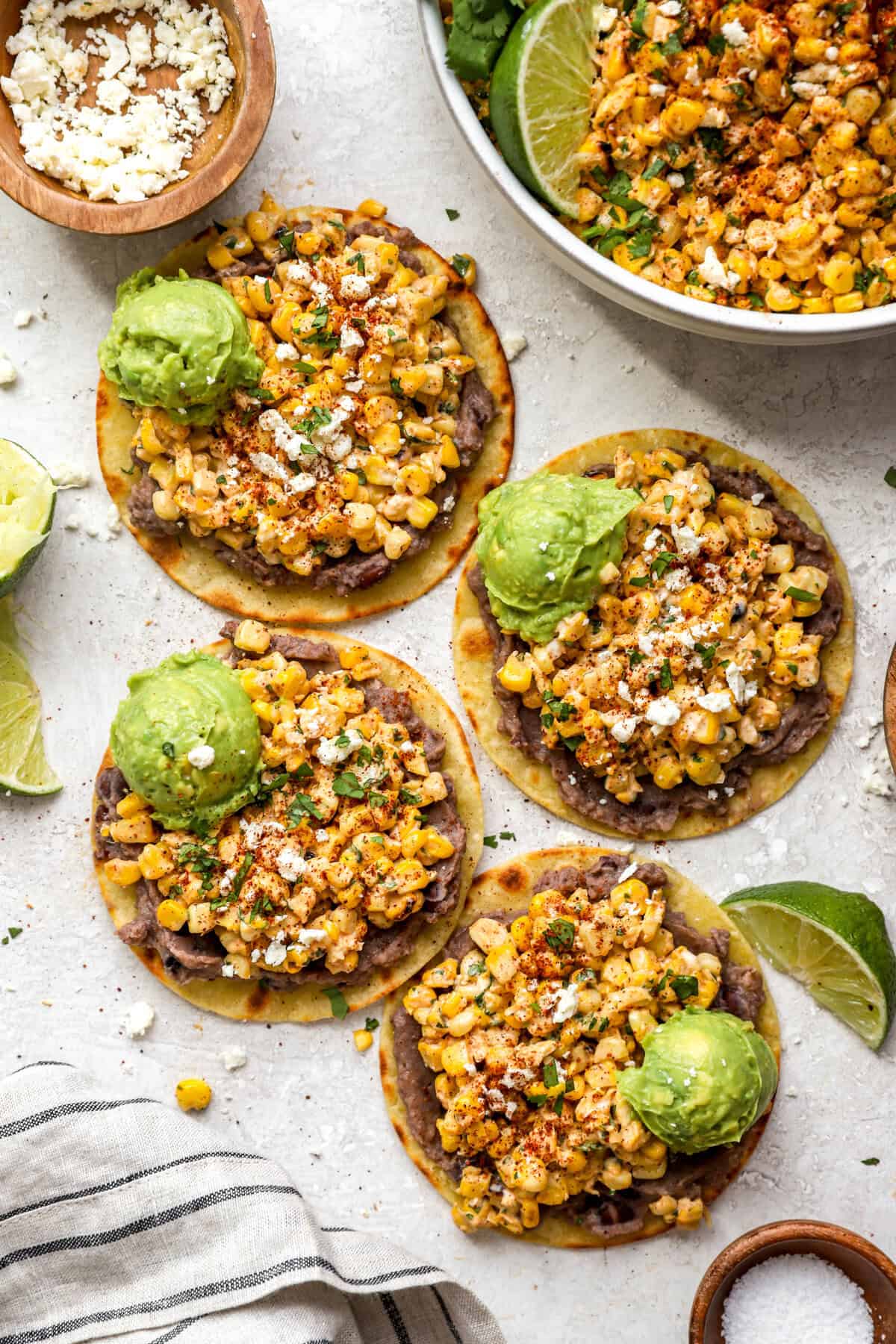 above image of four homemade tostadas topped with street corn salad, avocado, and cheese.