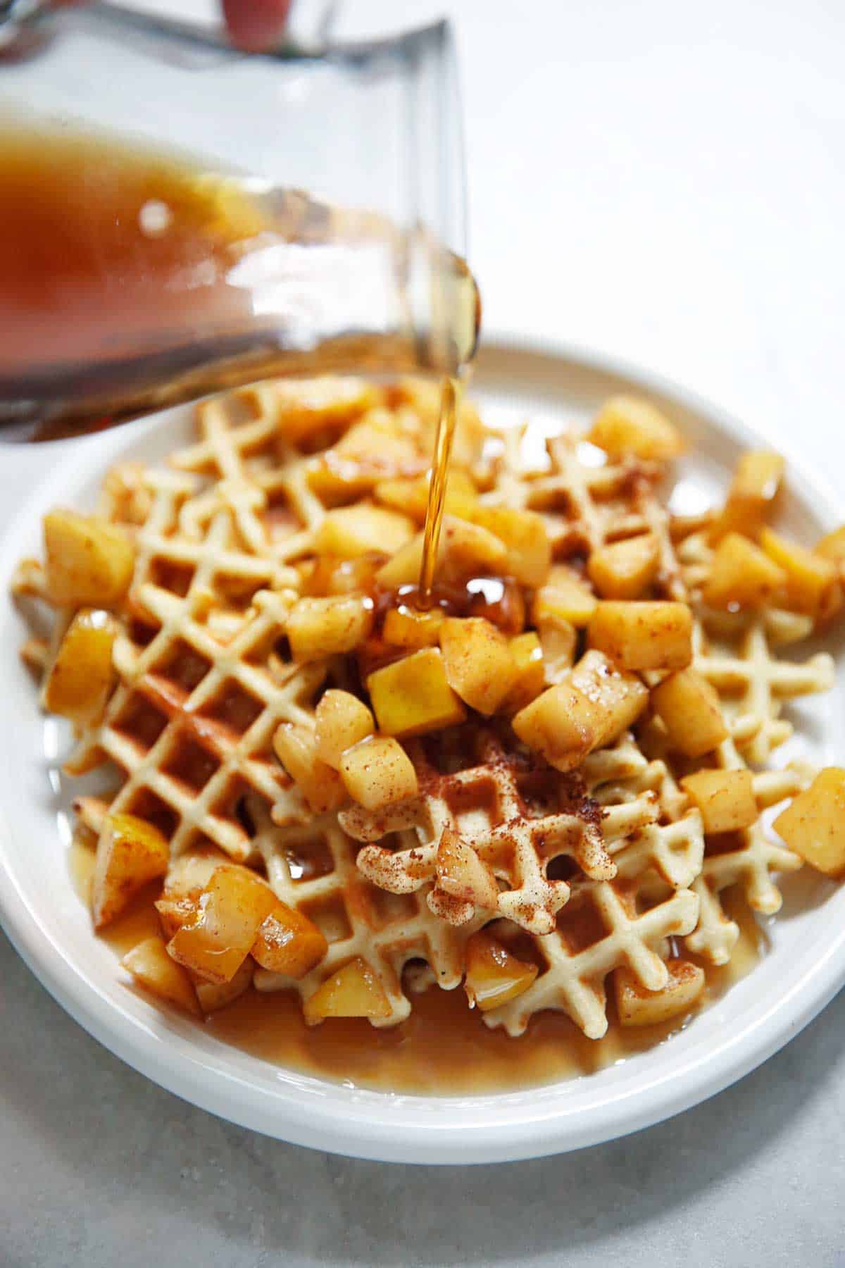 Mini waffles on a plate with apples and maple syrup.