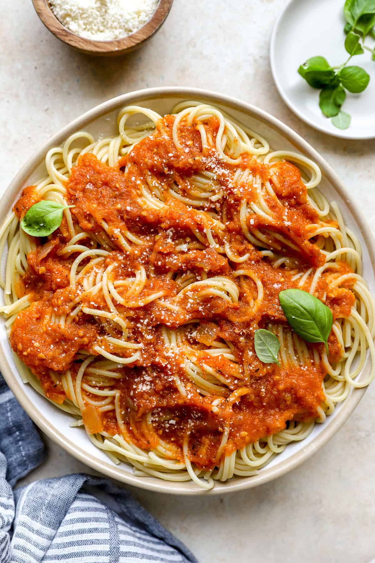 a cream bowl full of spaghetti noodles topped with the fresh tomato sauce, parmesan cheese and basil. 