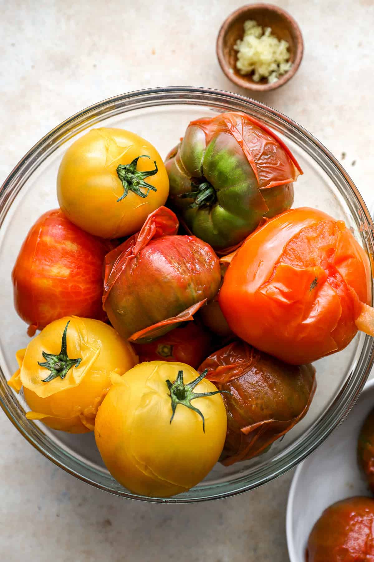 a glass bowl full of cooked tomatoes that are beginning to peel.