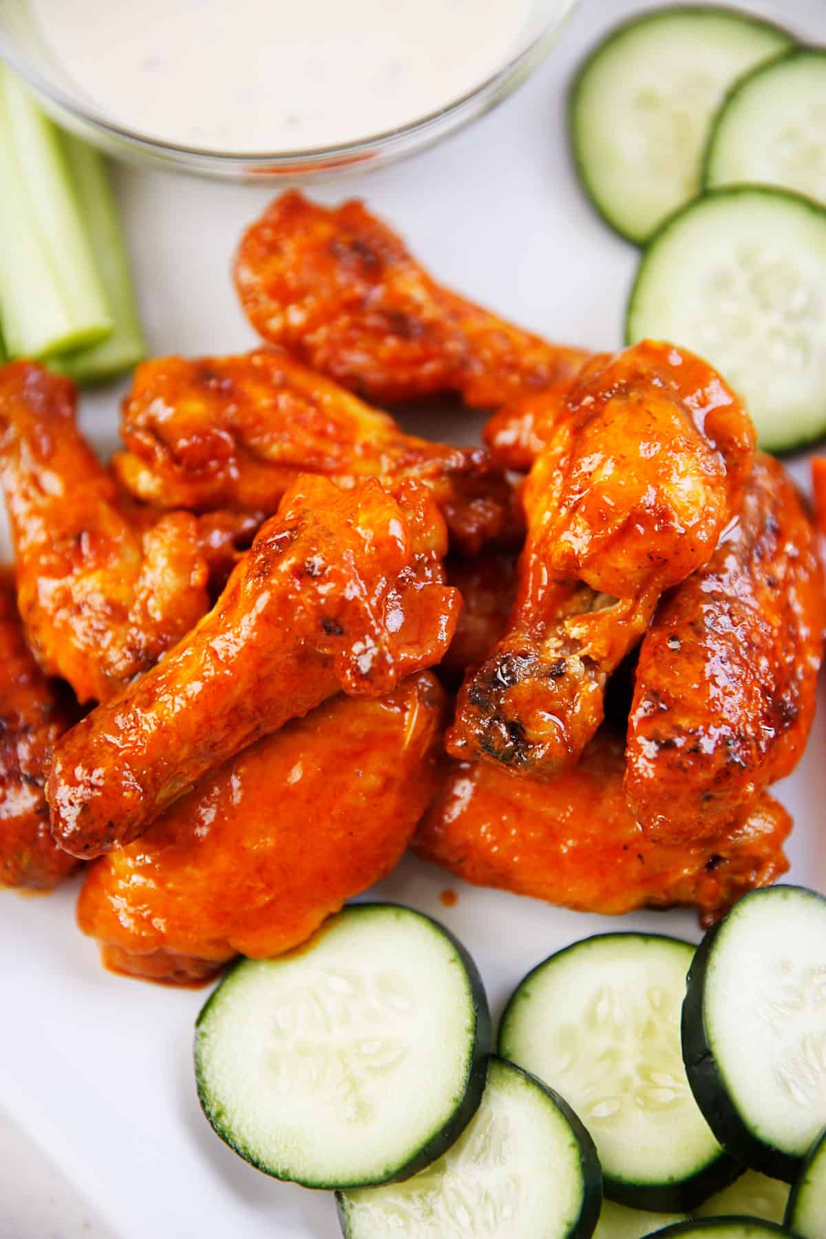 Saucy baked buffalo wings on a platter next to veggies and dip.