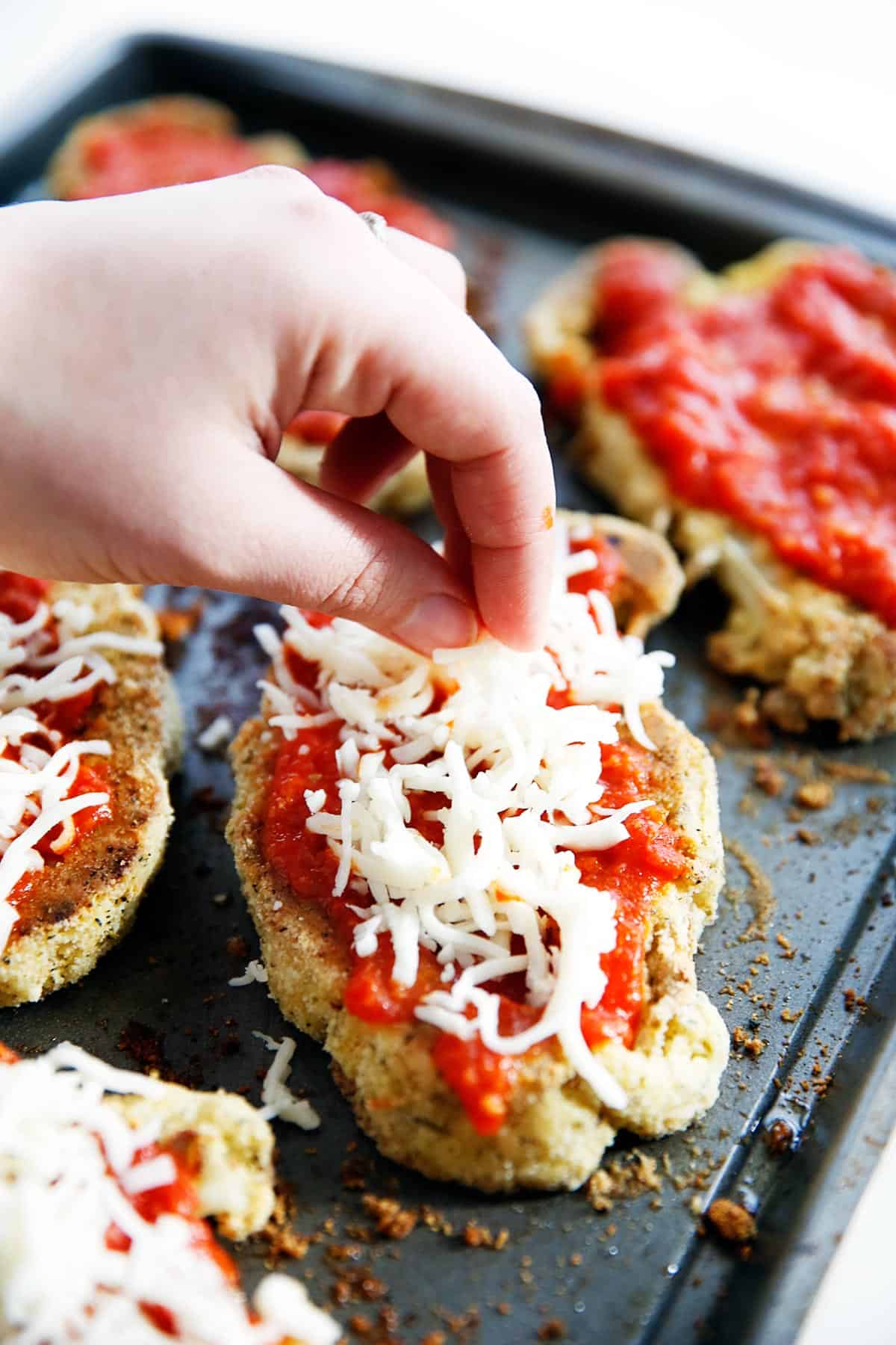 cheese being sprinkled over breaded cauliflower steaks topped with sauce.