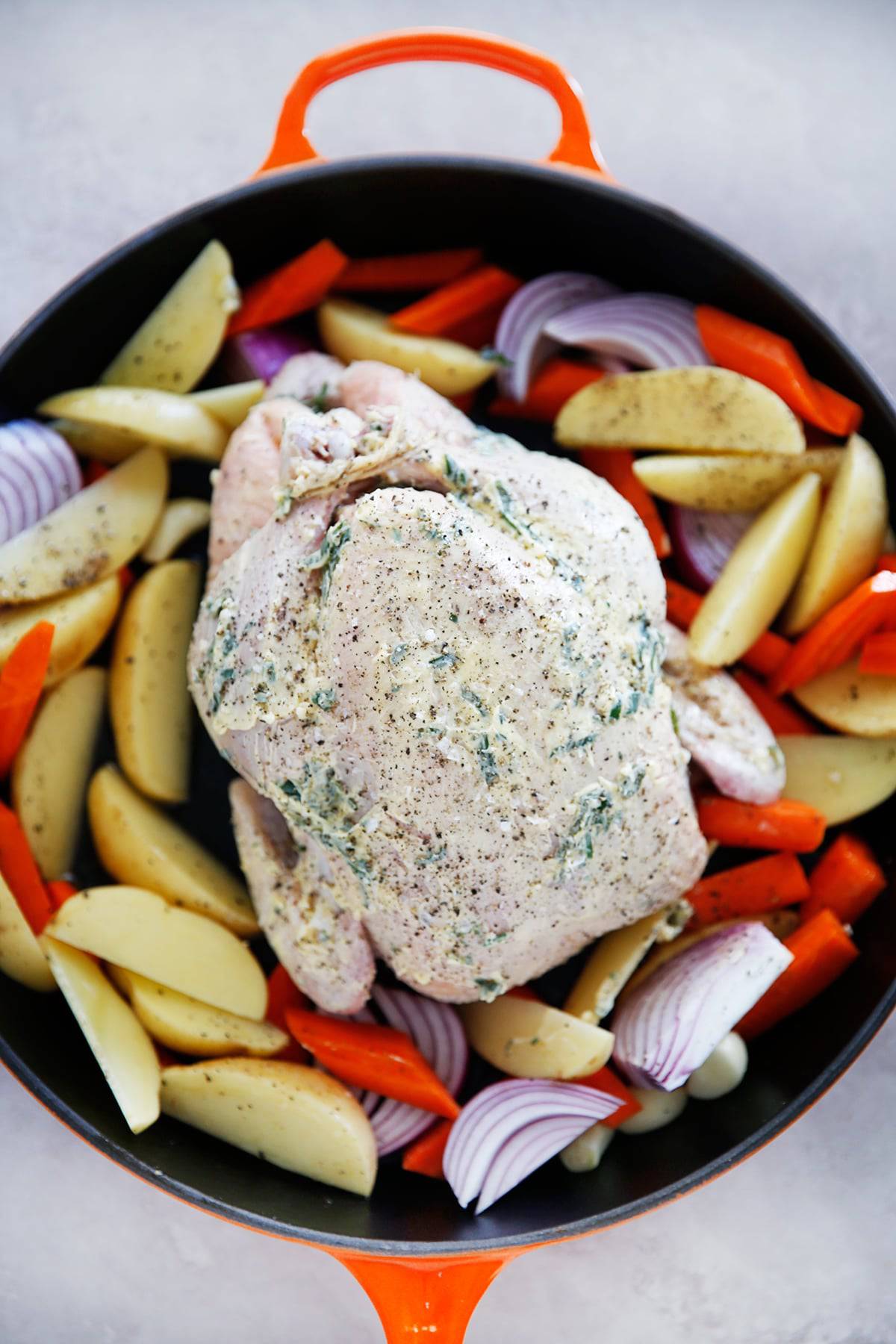 a whole chicken smothered in garlic butter surrounded by onion, potato, and carrot.