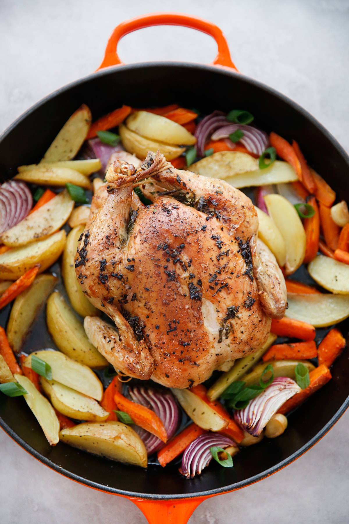 a whole roasted chicken in a pan surrounded by roasted veggies.