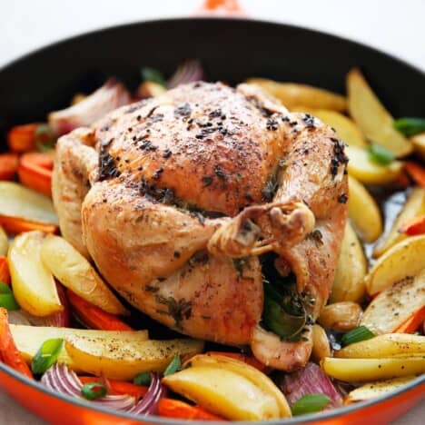 a roasting pan with a whole roast chicken surrounded by veggies from the side.
