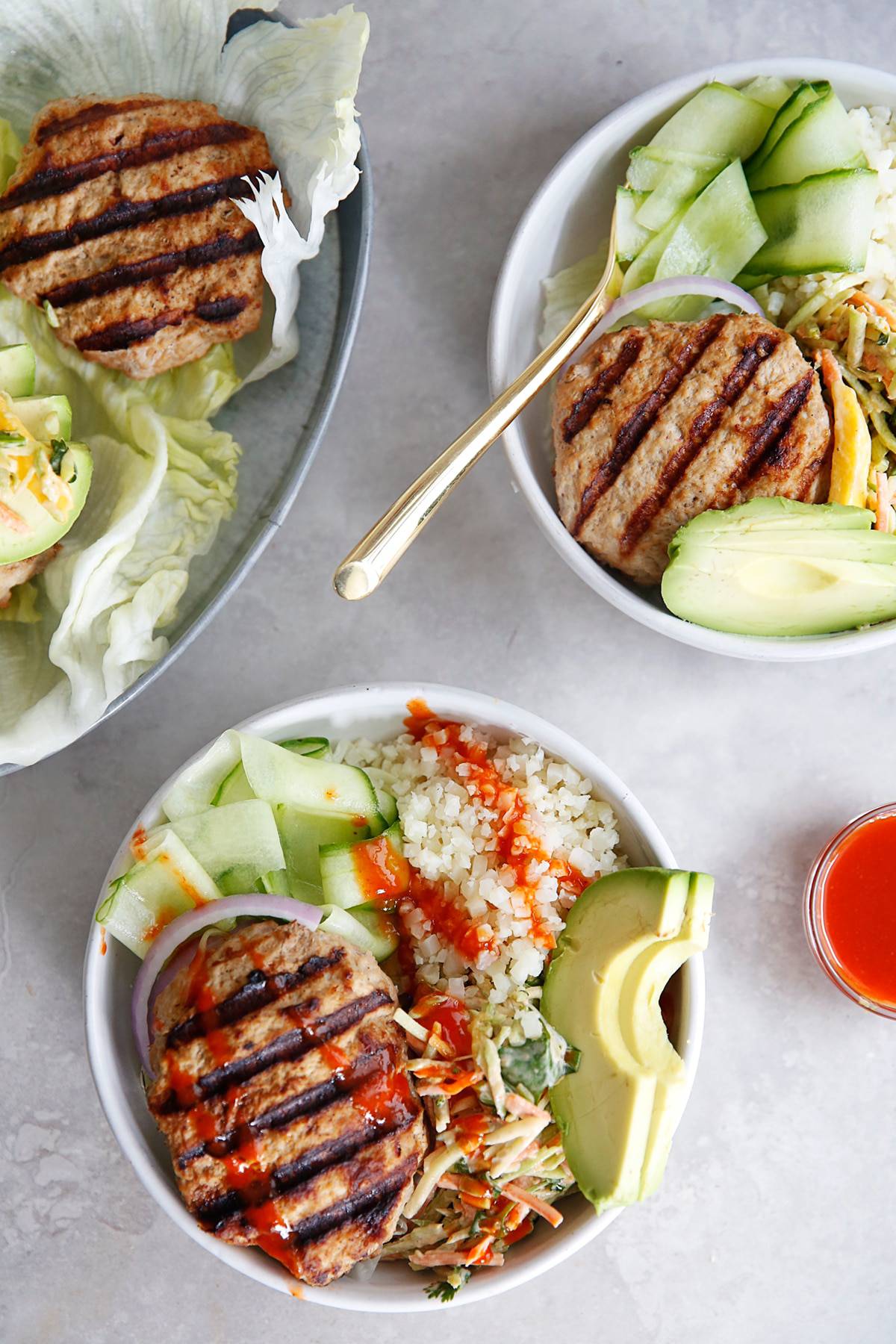 two burger bowls with avocado, cauliflower rice, and Sriracha overhead.