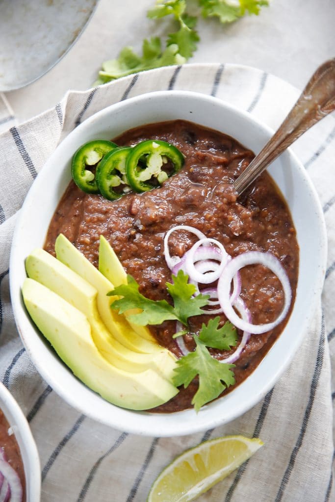 Black bean soup in a bowl with sliced avocados and peppers.
