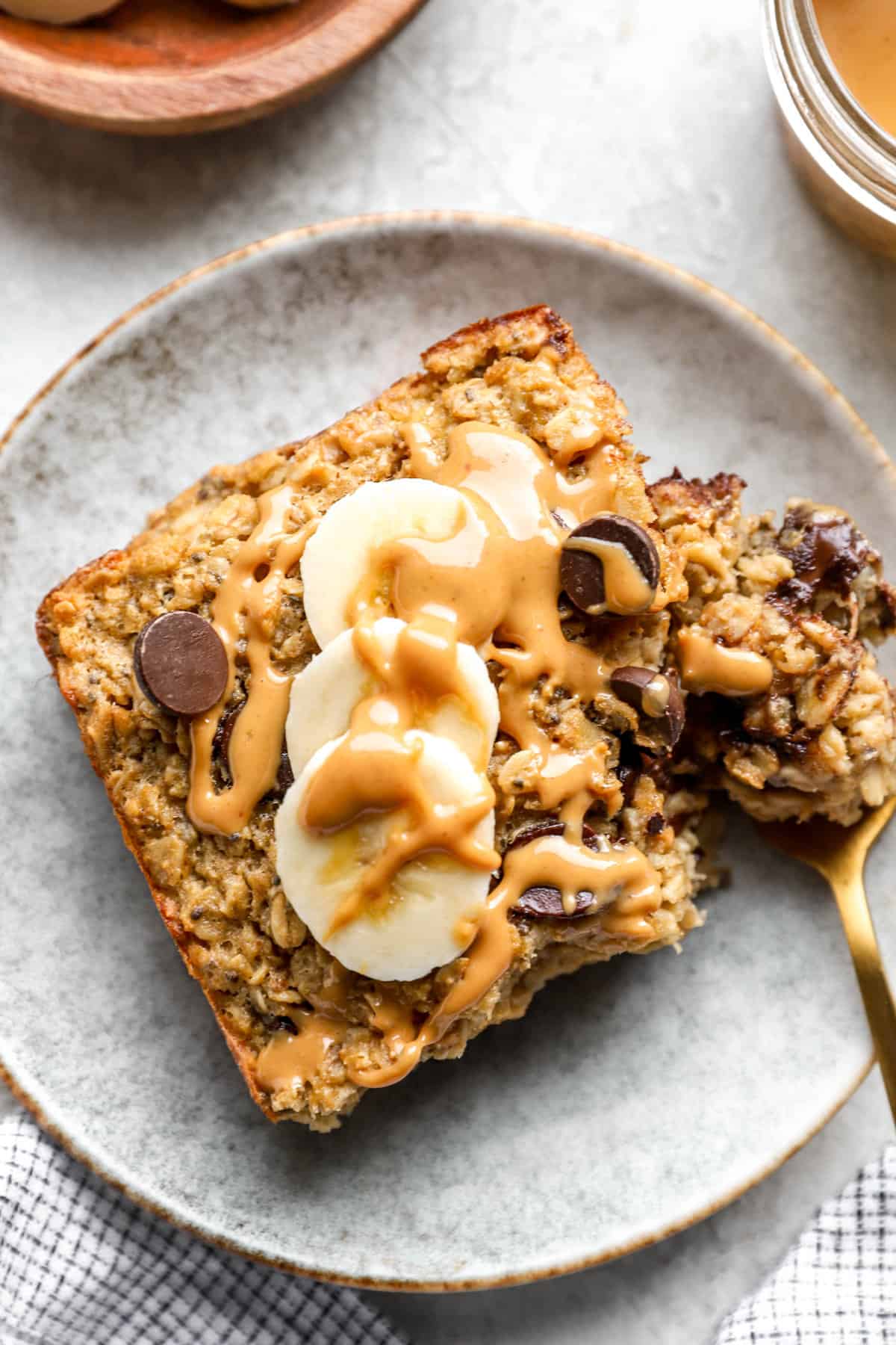above image of a fork scooping a chunk off of a slice of baked oatmeal topped with bananas and peanut butter.