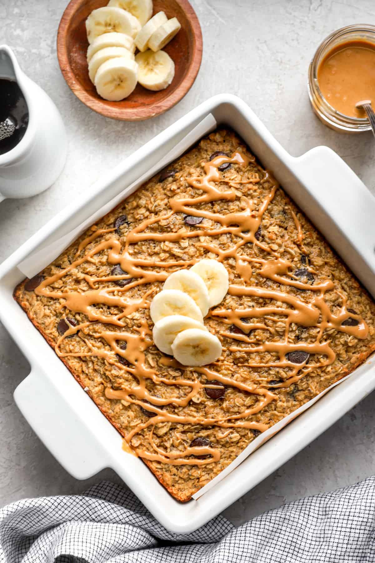a square baking dish filled with a baked oatmeal recipe with sliced banana layered in the center.