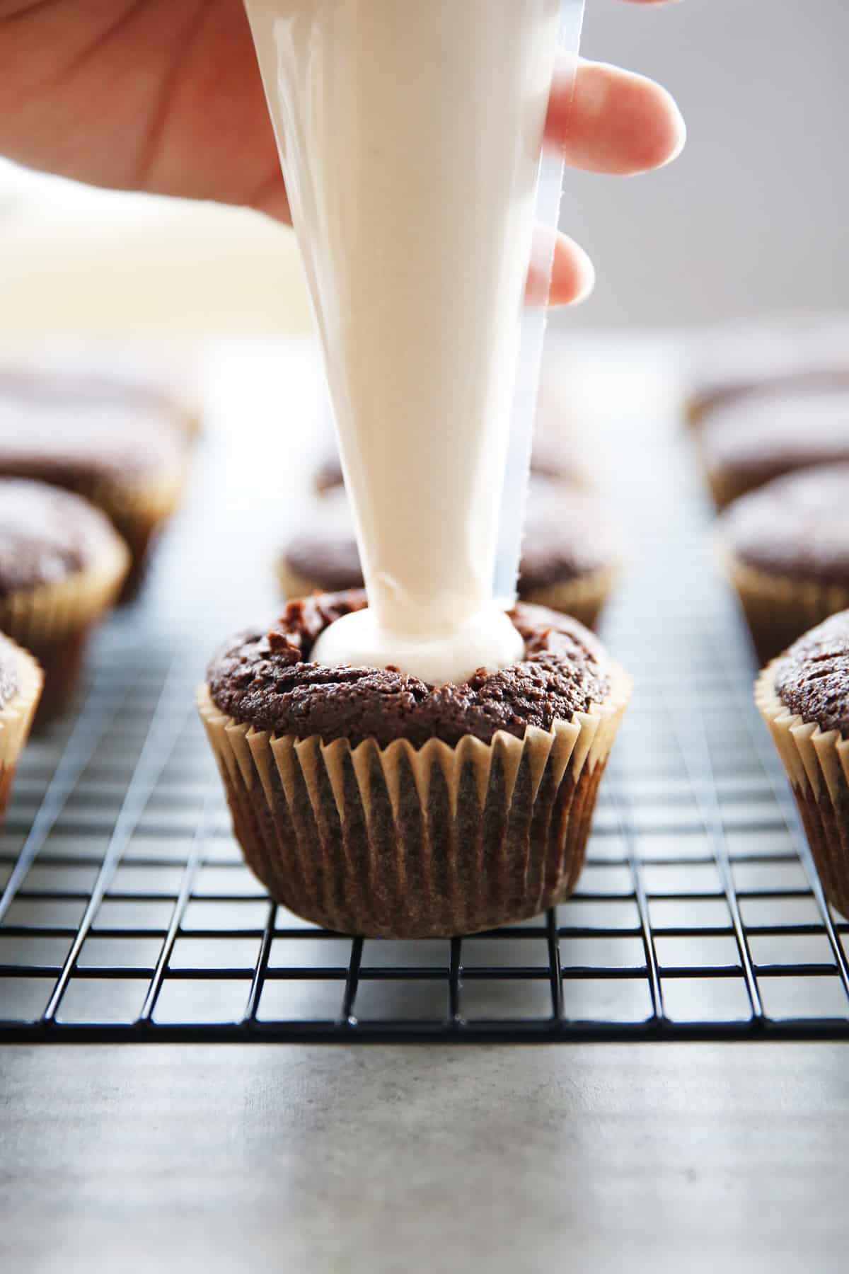 marshmallow cream being piped into a chocolate cupcake.