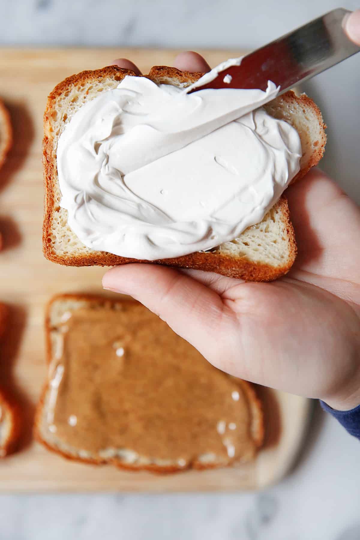 marshmallow fluff being spread on a slice of bread.