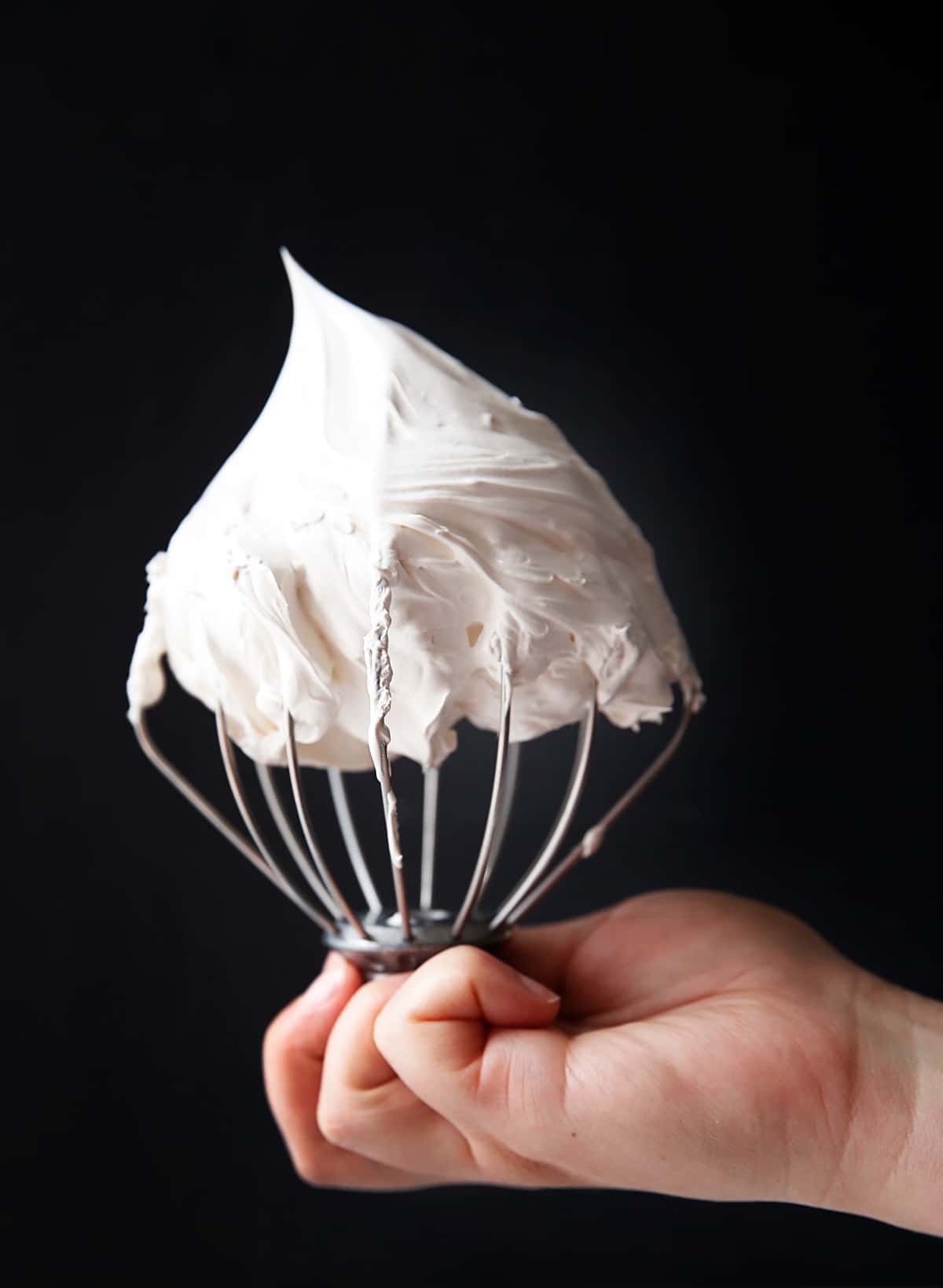 a whisk covered with marshmallow fluff held.