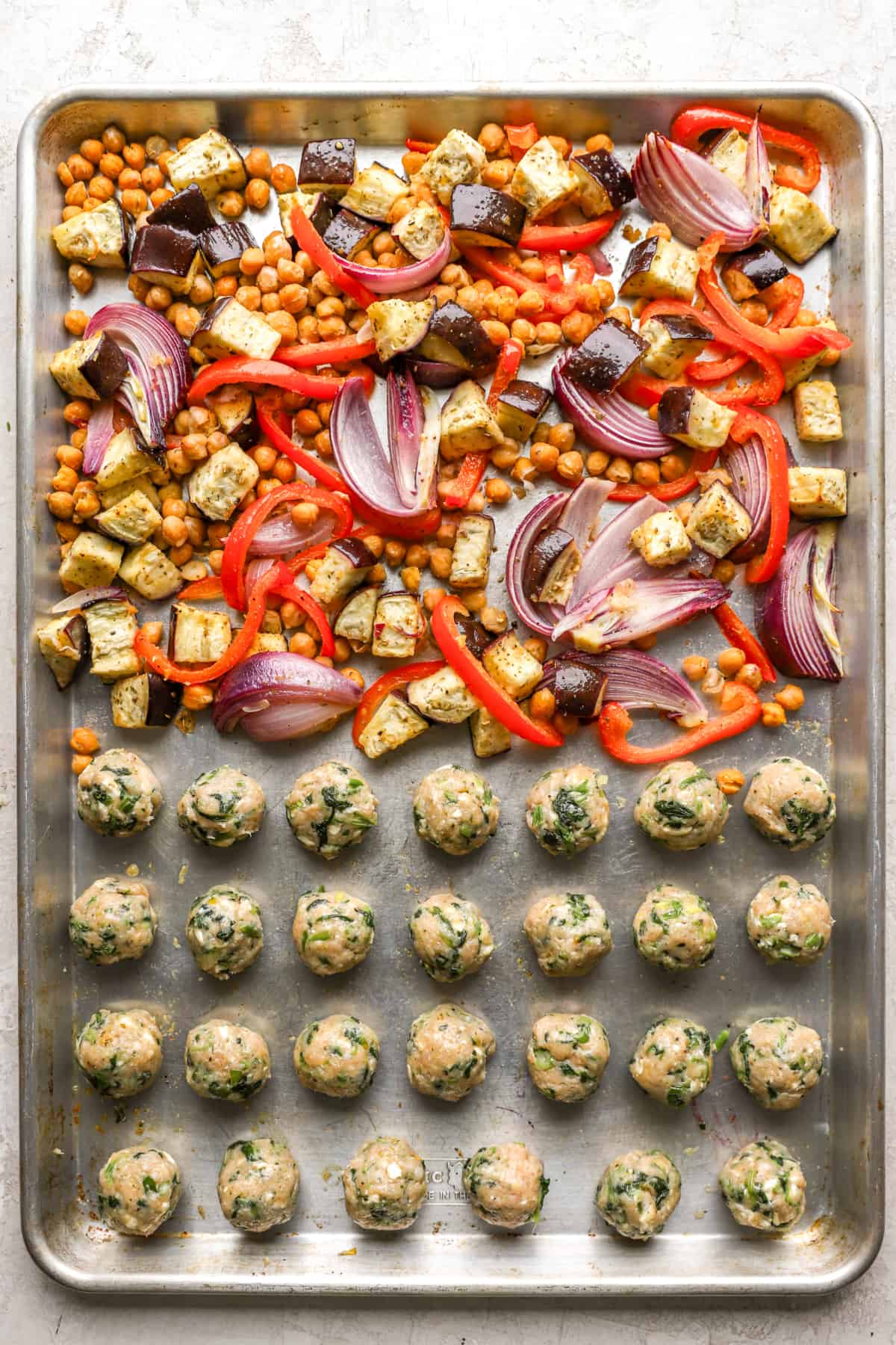 above image of chicken meatballs lined on a baking sheet with veggies and chickpeas.