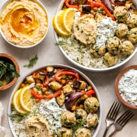 above image of two plates filled with greek chicken meatballs, roasted chickpeas, veggies, and hummus.
