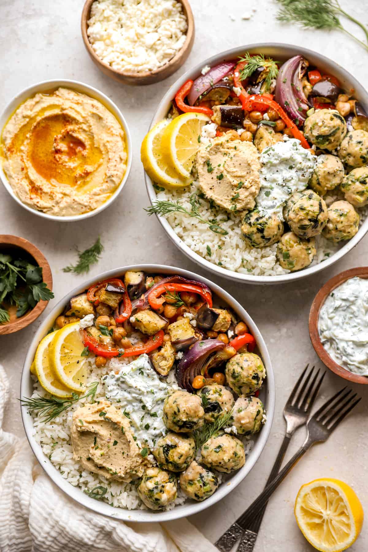 above image of two plates filled with greek chicken meatballs, roasted chickpeas, veggies, and hummus. 