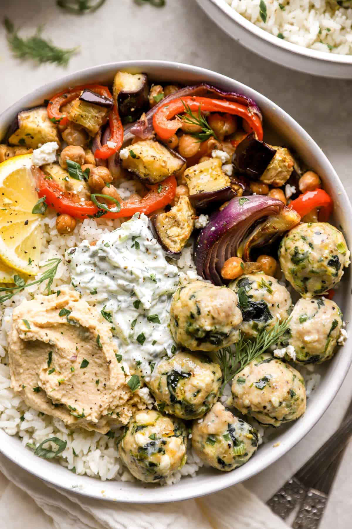 above image of a plate filled with greek chicken meatballs, roasted chickpeas, veggies, and hummus.
